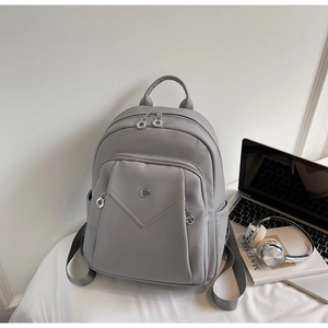 Detail of grey pebbled leather backpack showing silver zippers and front pocket with logo