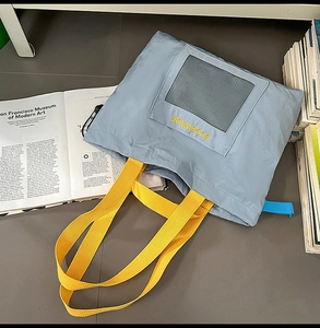 Detail of light blue tote bag featuring black mesh pocket and yellow branded handle straps