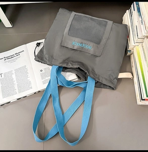 Close-up of charcoal nylon tote bag featuring a blue woven strap and front mesh pocket