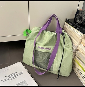 Detail of light green nylon tote bag featuring purple embroidery and black mesh pocket
