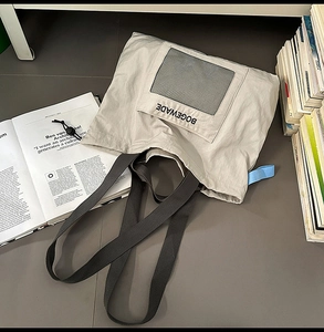 Detail of grey nylon tote bag with black mesh pocket and minimalist brand logo