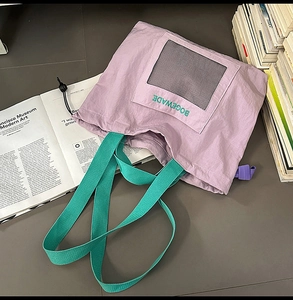 Detail of purple tote bag with green straps and mesh pocket against art books