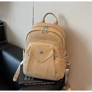Close-up of beige lychee grain leather backpack on book with silver hardware details