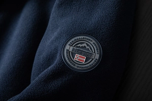 Detail of navy blue fleece jacket showing the circular Norway flag rubber badge texture