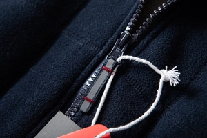 Detail of a black fleece jacket showing a resin zipper and gray-red woven puller