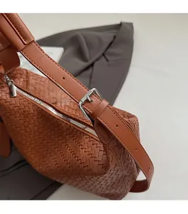 Detail of woven texture on caramel brown leather bag with silver metal buckle