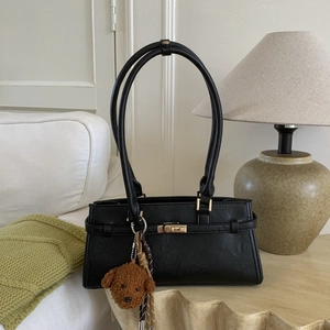 Close-up of black leather handbag featuring a gold twist lock and a cute teddy charm