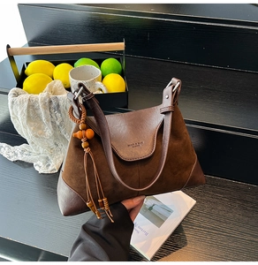 Detail of dark brown suede saddle bag featuring branded embossing and wooden gourd charm