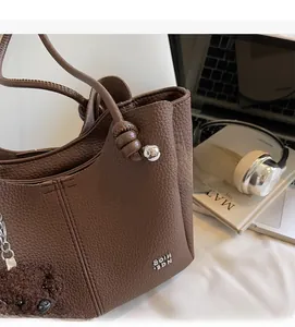Dettaglio borsa tote in pelle marrone scuro con trama litchi, logo argento e ciondolo orso