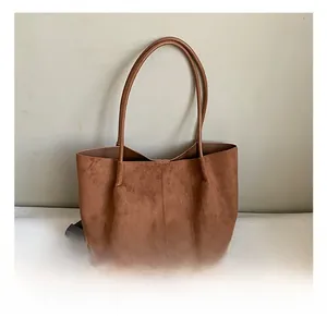 Close-up of brown suede tote bag featuring slim leather handles in a minimalist lifestyle setting