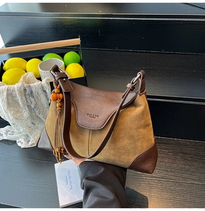 Detail of suede crossbody bag with brand embossing and wooden bead tassel ornament