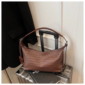 Detail of brown woven leather hobo bag with zip closure on silver suitcase