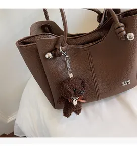 Dettaglio della borsa a secchiello marrone scuro con ciondolo a forma di orsetto di peluche