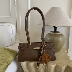 Close-up of brown faux leather shoulder bag with gold turn-lock and plush bear charm