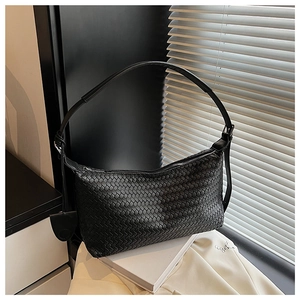 Detail of black hand-woven hobo bag with intricate texture and silver zipper on white books