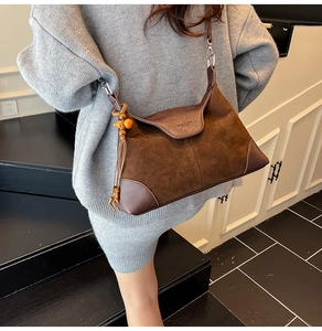 Detail of retro brown suede crossbody bag with leather patchwork and tassel charm