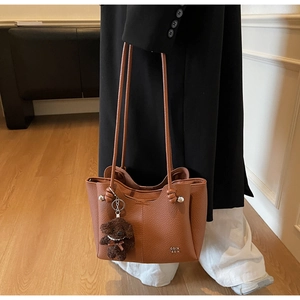 Dettaglio borsa shopper marrone con texture a grana e ciondolo orsetto su modella
