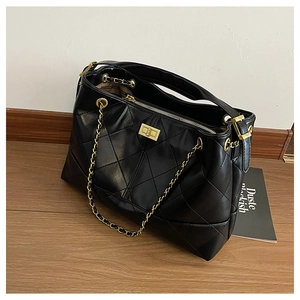 Detail of black quilted tote bag with gold twist lock and adjustable side buckles
