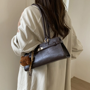Detail of dark brown leather shoulder bag with metallic clasp and cute plush bear charm