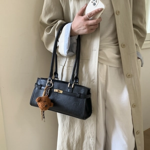 Close-up of black leather bag with metal turn-lock, cross straps and cute bear charm