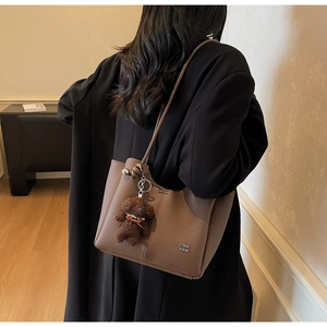 Dettaglio della borsa a secchiello in pelle marrone con ciondolo a orsetto e logo sul retro