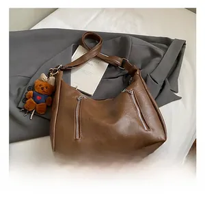 Detail of vintage brown leather hobo bag with twin vertical zippers and teddy bear charm