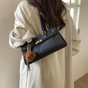 Detailed view of black leather shoulder bag featuring gold twist lock and bear charm