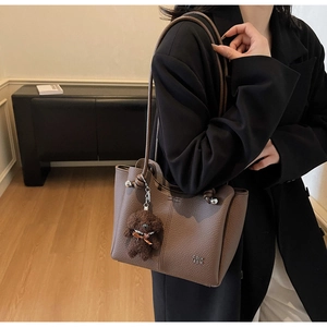 Dettaglio della borsa tote in pelle marrone con motivo litchi e ciondolo a orsetto