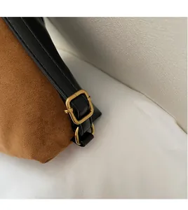 Detail of adjustable black leather strap with gold buckle on brown suede tote bag
