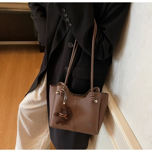 Dettaglio della borsa tote in pelle marrone con ciondolo a forma di orso e manico a nodo
