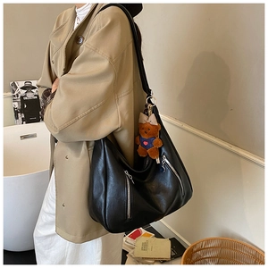 Close-up of black PU leather tote bag featuring side zippers and a cute teddy bear charm