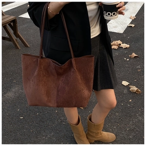 Close-up of a large brown suede tote bag carried by a model on an autumn city street