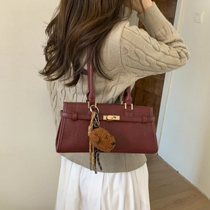 Detail of burgundy retro shoulder bag featuring a gold metal twist lock and bear charm