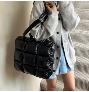 Close-up of black quilted down tote bag showing puffy grid stitching and thick shoulder strap