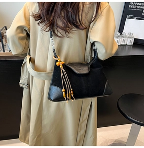 Detail of black suede patchwork shoulder bag with wooden bead tassel on a khaki coat