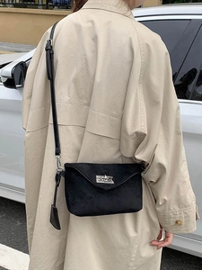 Minimalistische schwarze matte Umhängetasche mit Silberverschluss zu einem beigen Trenchcoat