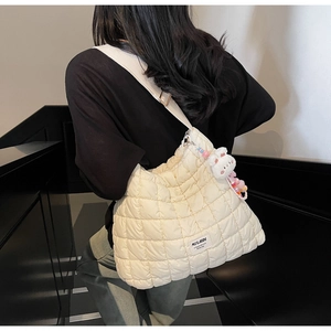 Detail of white quilted tote bag with bear charm and beaded keychain on shoulder