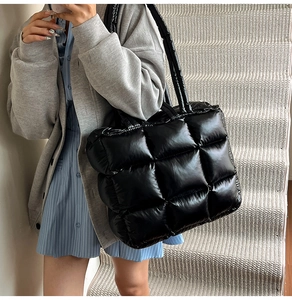 Detail of glossy black quilted puffer tote bag featuring soft padded texture and top handles