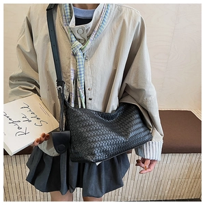 Detail of black woven shoulder bag with leather strap and decorative heart pendant