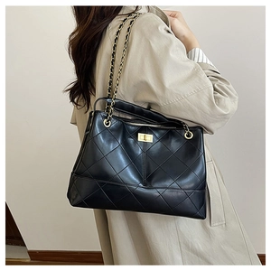 Detail of black quilted tote bag with gold twist lock and elegant metal chain strap