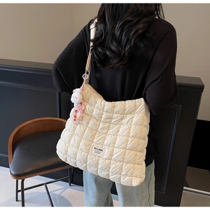Close-up of white quilted tote bag with pink bunny charm on black attire