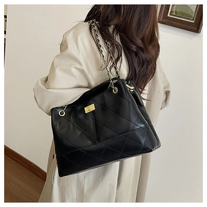 Detail of black quilted tote bag with gold twist lock and chain strap on a model