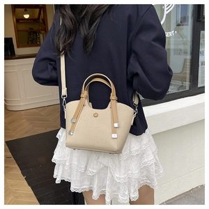 Close-up of beige woven bucket bag with brown leather trim held by model in cafe setting
