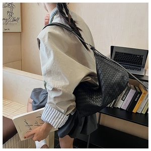 Detail of a large black woven leather hobo bag worn by a model in a modern office setting
