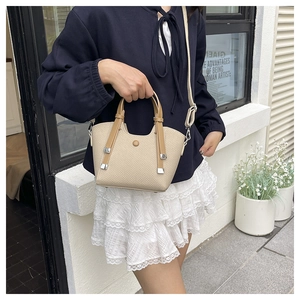 Close-up of beige woven textured bucket bag with brown leather handles and silver hardware