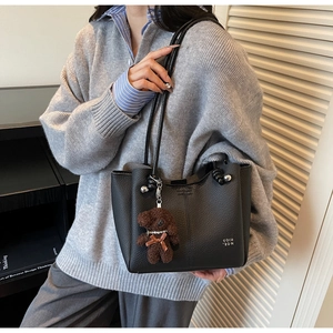 Dettaglio borsa a secchiello in pelle nera con ciondolo a forma di orsetto e logo