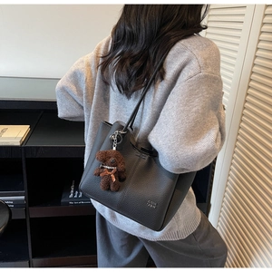 Dettaglio della borsa tote nera testurizzata con un ciondolo a forma di orsetto marrone