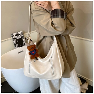 Detail of cream hobo bag with zipper decor and a cute teddy bear charm on the strap
