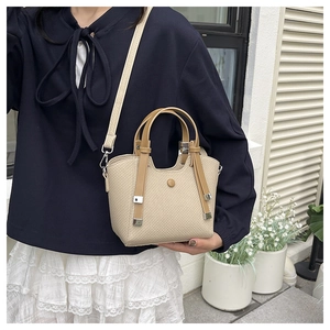Chic beige woven bucket bag with brown handles carried by a model in a trendy outfit