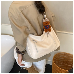 Detail of a large cream hobo bag with silver zippers and a brown plush bear charm
